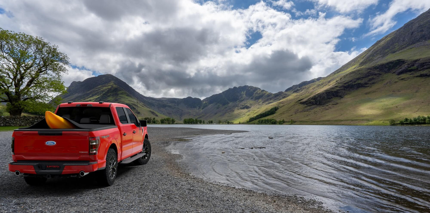 Silver Ford F-150 with Sawtooth Stretch tonneau covering orange kayak in a beautiful mountain lake sunset