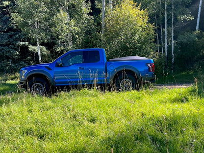 Blue Ford Raptor with Sawtooth Stretch tonneau expanded over short cargo load in the forest