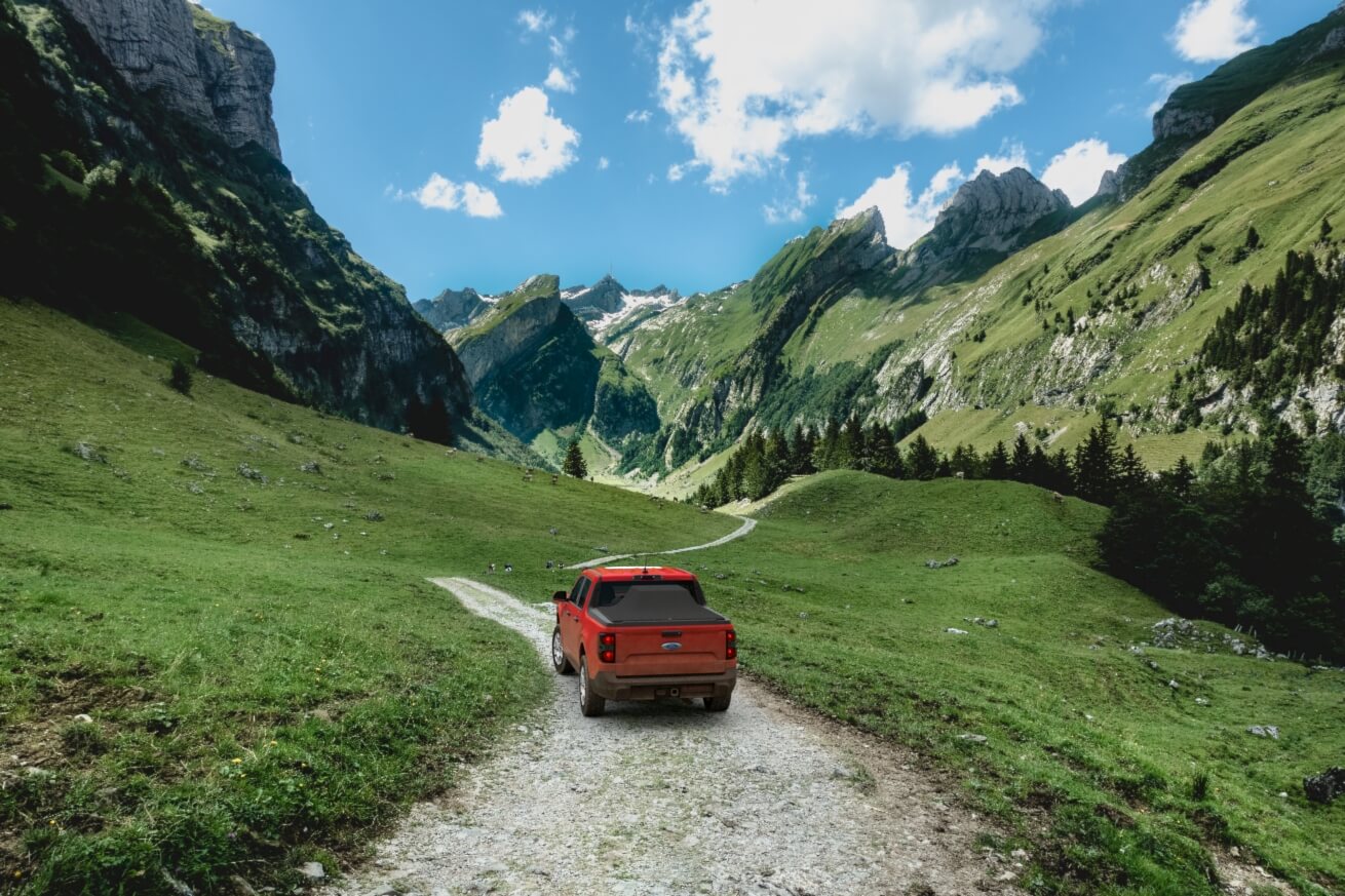 Red 2024 Ford Maverick with Sawtooth Stretch tonneau expanded over tall cargo load in narrow green mountain valley